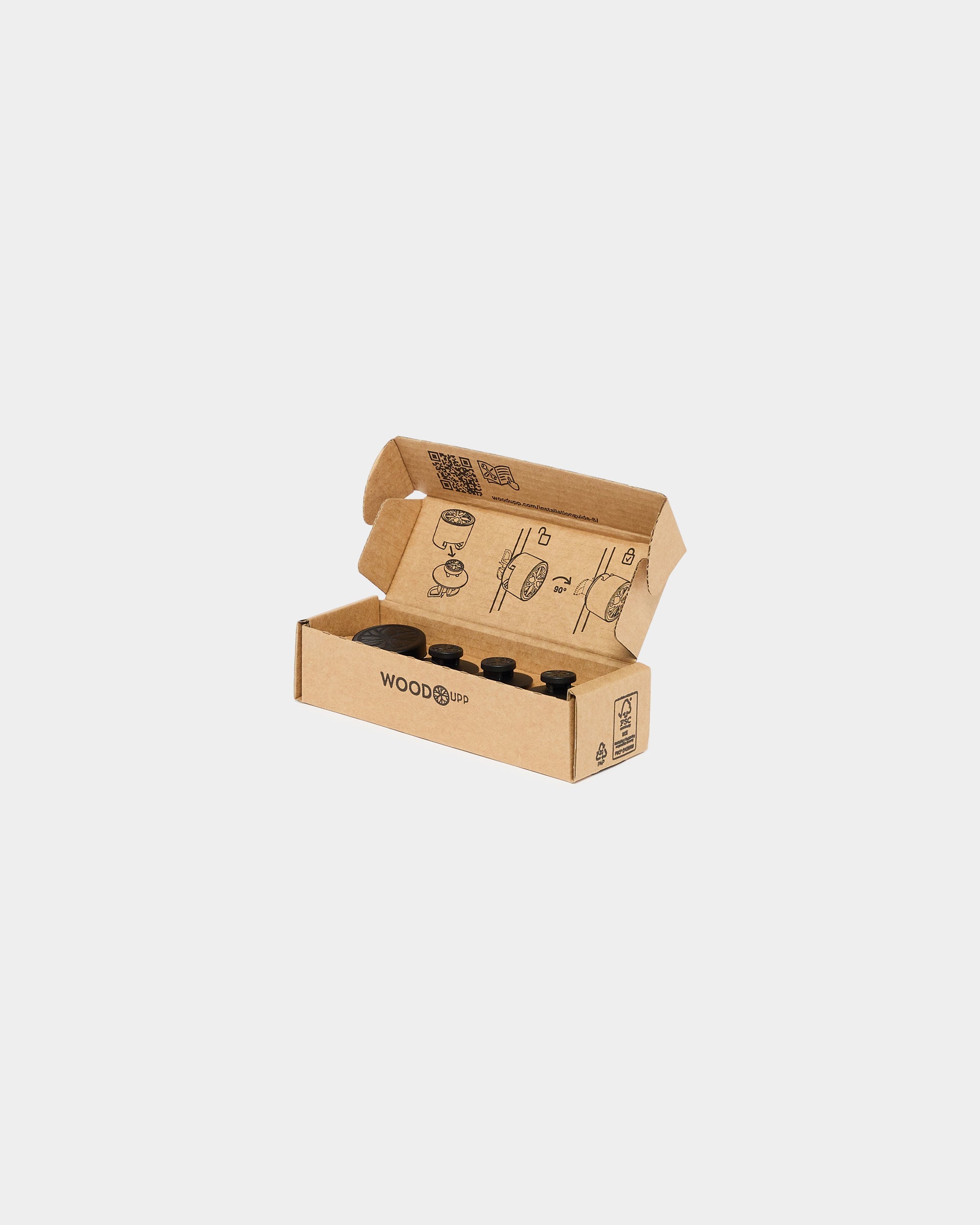 Open cardboard box with WoodUpp branding containing four black cylinders for acoustic panel installation and assembly instructions printed inside the lid.